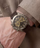 A close-up of a wrist wearing a guess chronograph watch with a dark brown leather strap, a brushed steel case, and a dark dial with gold subdials.