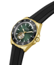 A Guess Automatic watch with a gold-tone case, black bezel, green dial, and black textured strap, shown on a clean white background. lifestyle