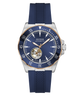 Guess Automatic watch with a blue dial, blue bezel, and blue textured strap, featuring a silver-tone stainless steel case with a gold-tone rotating bezel and a visible tourbillon movement.