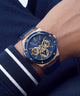 A wristwatch with a blue dial and blue strap, featuring a rose gold-toned case and gold details, shown worn on a person's wrist.