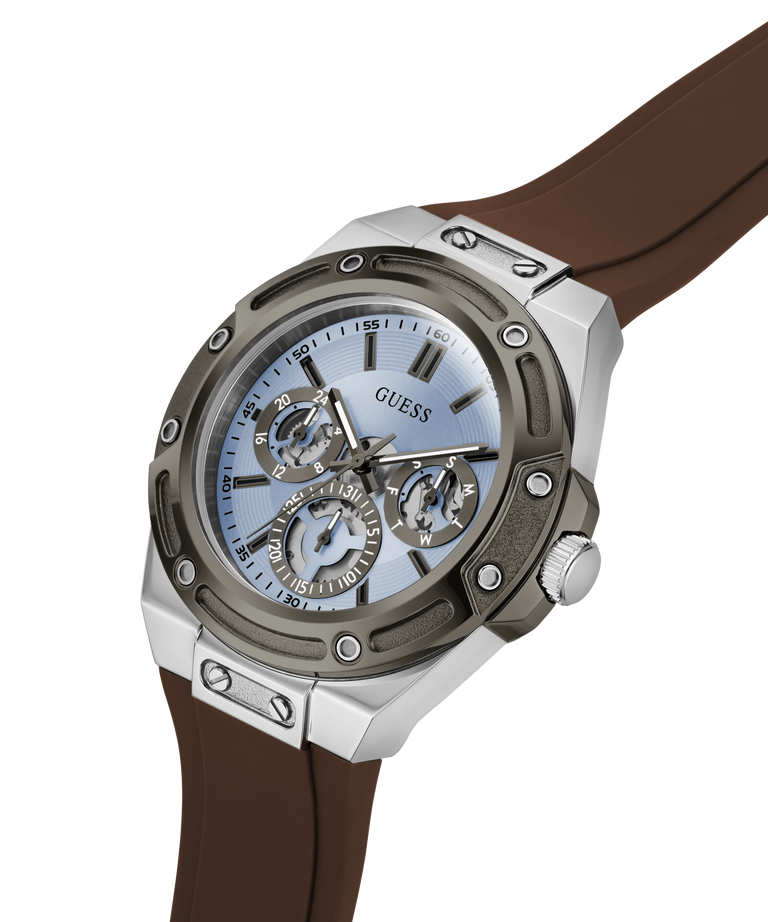 A GUESS men's watch featuring a silver-toned stainless steel case, a light blue dial with skeletonized subdials, and a brown rubber strap, shown on a clean white background. lifestyle