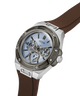 A GUESS men's watch featuring a silver-toned stainless steel case, a light blue dial with skeletonized subdials, and a brown rubber strap, shown on a clean white background. lifestyle