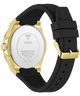 Back view of a Guess watch with a gold-tone case and a black textured silicone strap, showing the stainless steel case back with GUESS branding.