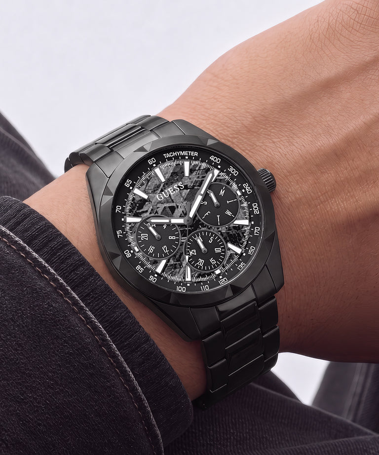 A close-up of a black dial steel chronograph watch with a matching black metal link bracelet, worn on a person's wrist.