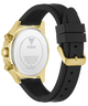 A GUESS watch shown from the back, featuring a gold-tone case, a white backplate with brand text, and a black silicone strap with a gold buckle.