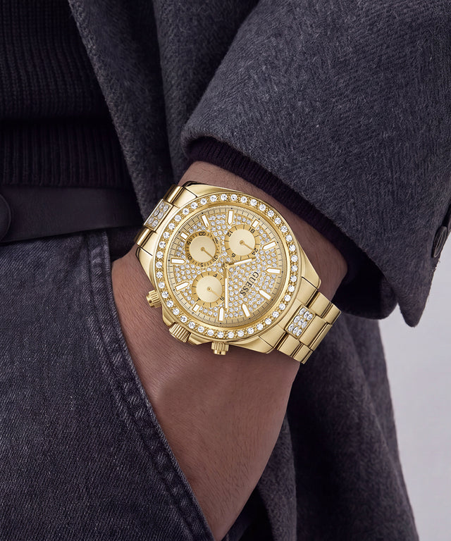 A gold-tone GUESS chronograph watch with a diamond-encrusted bezel and matching bracelet, shown worn on a person's wrist.