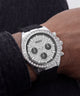 A close-up of a Guess wristwatch with a silver-tone case, diamond-encrusted bezel and dial, black subdials, and a black rubber strap worn on a person's wrist.