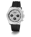 A Guess wristwatch with a silver-tone case, a bezel set with clear stones, a textured black dial with three black subdials, and a black silicone strap, shown on a white background.