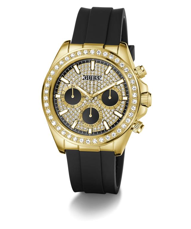 A luxury wristwatch by Guess featuring a gold-tone case encrusted with clear crystals, a black dial with three subdials, and a black silicone strap, shown against a plain white background.