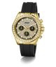 A luxury wristwatch by Guess featuring a gold-tone case encrusted with clear crystals, a black dial with three subdials, and a black silicone strap, shown against a plain white background.