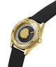 A luxury wristwatch by Guess featuring a gold-tone case with a textured bezel, crystal accents, and a central gold lion head on a dark sunburst dial. The watch is fitted with a black rubber strap and photographed on a clean white background. lifestyle