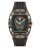 A GUESS wristwatch with a dark gray and black case, a colorful neon sugar skull face graphic, and a perforated black rubber strap with yellow and orange stitching.