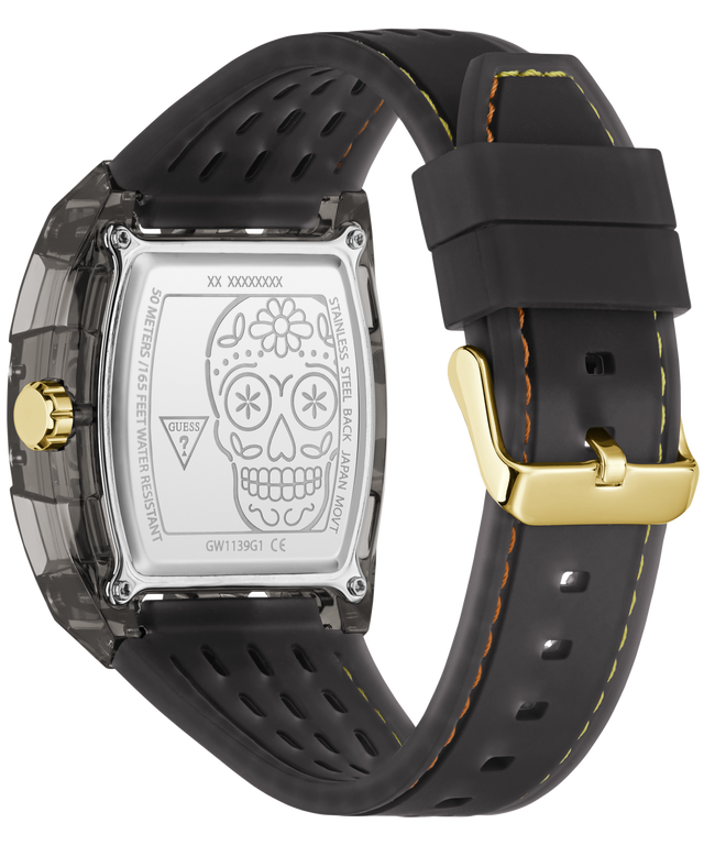 Back view of a GUESS watch with a transparent case, silver engraved back plate featuring a sugar skull design, and a black silicone strap with yellow stitching and a gold buckle.