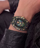 A close-up lifestyle shot of a wrist wearing a rugged black watch with gold accents and a colorful neon skull dial, set against a dark leather background.
