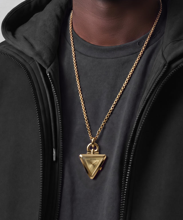 A gold-tone Guess triangle pendant necklace worn by a model over a dark gray t-shirt and black zip-up hoodie. 