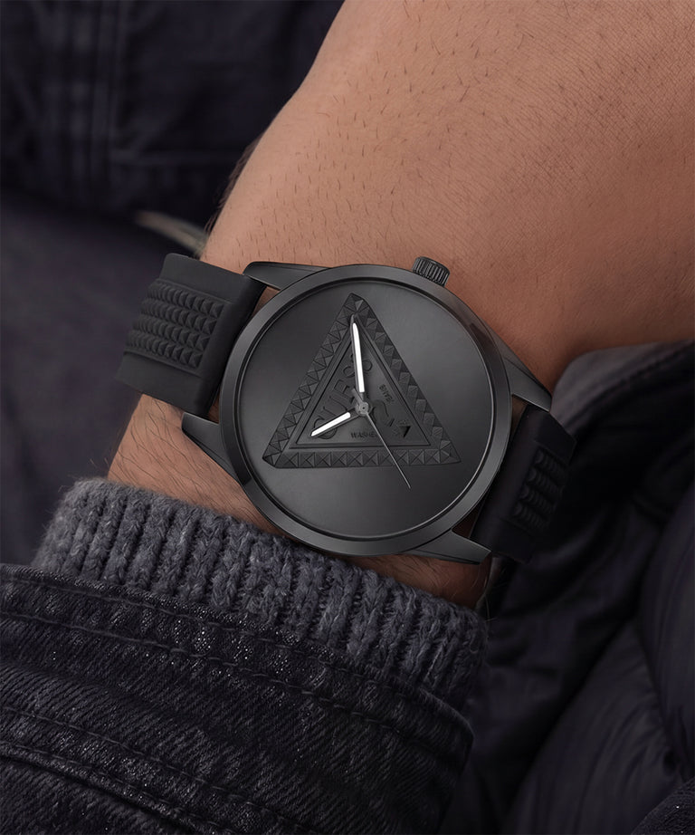 A close-up of a black analog watch with a textured triangular dial and black strap, worn on a person's wrist.