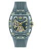 A GUESS wristwatch with a translucent smoky gray case and matching textured strap, featuring gold-tone accents, gold Arabic numerals, and two smaller subdials on a white background.