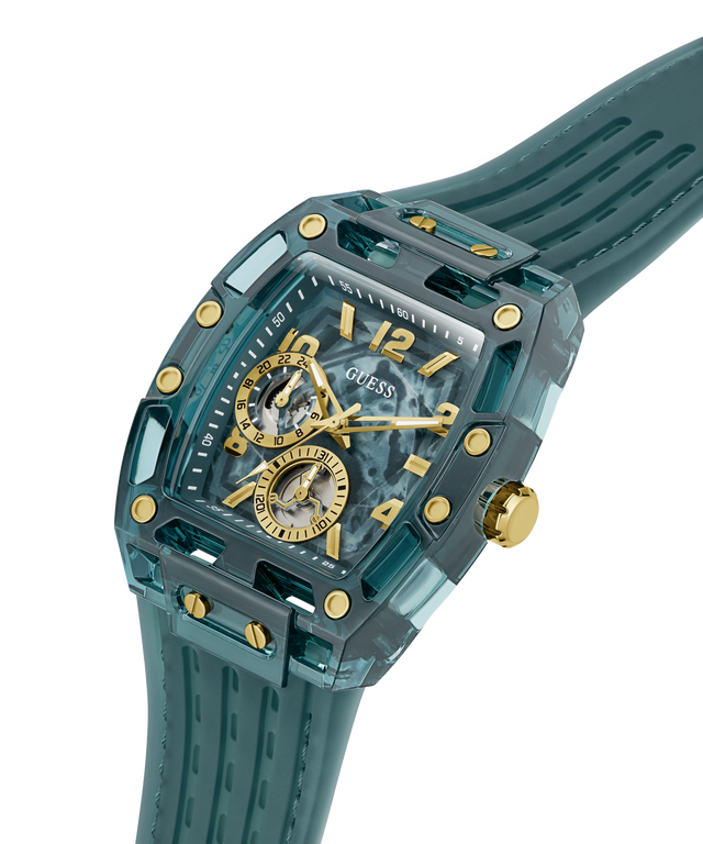A GUESS wristwatch with a translucent teal resin case, matching strap, gold-tone accents, and a skeleton dial showing the inner movement, photographed on a clean white background. lifestyle