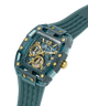 A GUESS wristwatch with a translucent teal resin case, matching strap, gold-tone accents, and a skeleton dial showing the inner movement, photographed on a clean white background. lifestyle