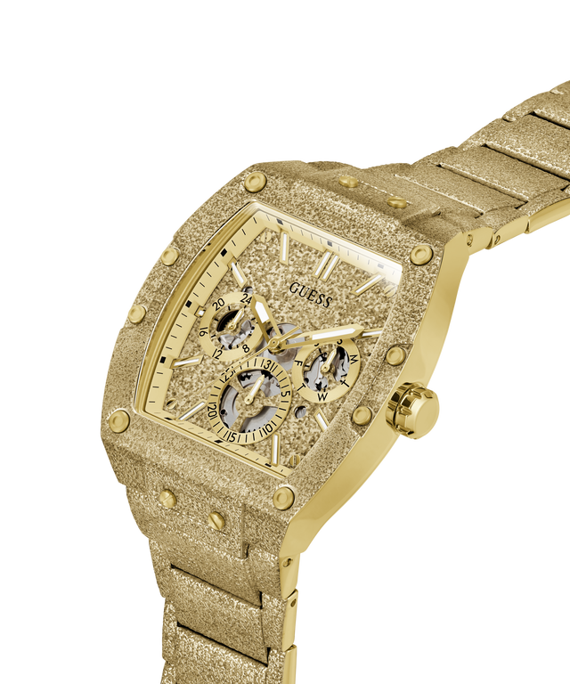 A gold-tone Guess wristwatch with a textured, glittery gold case and matching metal bracelet, featuring a multi-dial skeleton dial on a white background. lifestyle