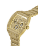 A gold-tone Guess wristwatch with a textured, glittery gold case and matching metal bracelet, featuring a multi-dial skeleton dial on a white background. lifestyle