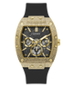 A luxury wristwatch by Guess featuring an ornate gold-tone case with a textured bezel, a black multi-dial dial, and a black rubber strap, shown against a plain white background.