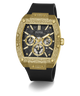 A luxury wristwatch by Guess featuring a textured gold-tone case, a black dial with three subdials, and a black rubber strap, shown on a clean white background.
