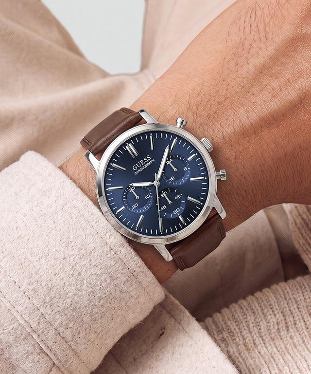 A wristwatch with a dark blue dial and brown leather strap worn on a person's wrist, framed by beige knit clothing.