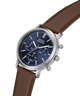 A GUESS chronograph watch with a silver-tone stainless steel case, a dark blue dial with three subdials, and a brown leather strap, shown on a plain white background. lifestyle