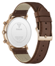 The back of a GUESS watch with a brown leather strap and a rose gold case, showing the branded white back plate and buckle.