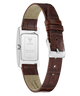 A close-up of a wristwatch strap on a white background, showing the back of a silver rectangular watch case with a brown leather strap and a silver buckle.