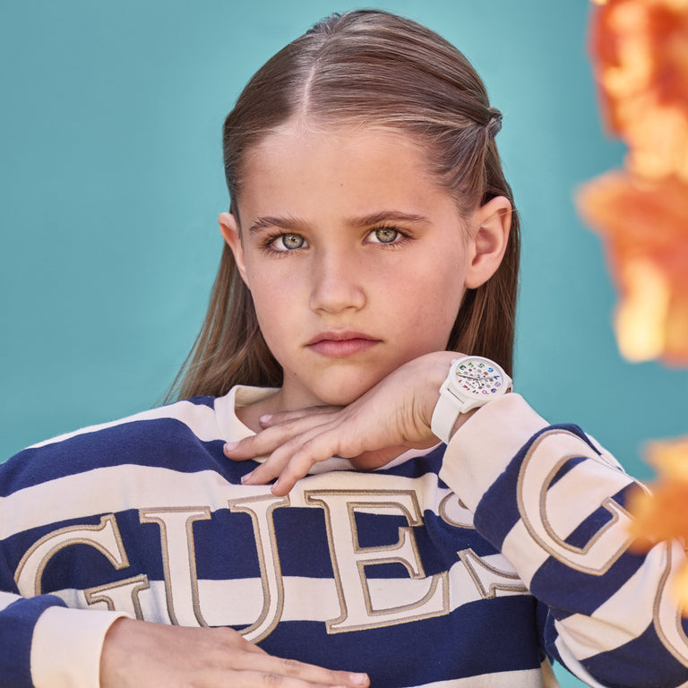 Young girl wearing a blue and white striped sweater with 'GUESS' branding against a teal background.