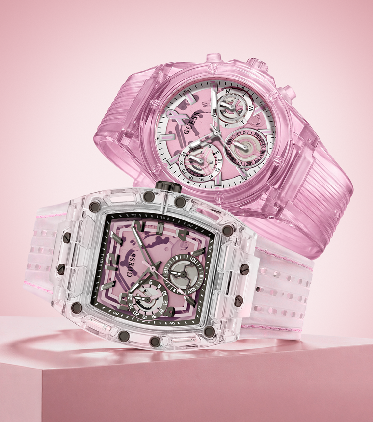 Two transparent pink watches displayed on a pink surface against a soft pink background. One watch is positioned in front in a square case with a skeletonized dial and visible pink movement, while the second watch is behind it in a rounded rectangular case, also showing a pink transparent strap and dial.