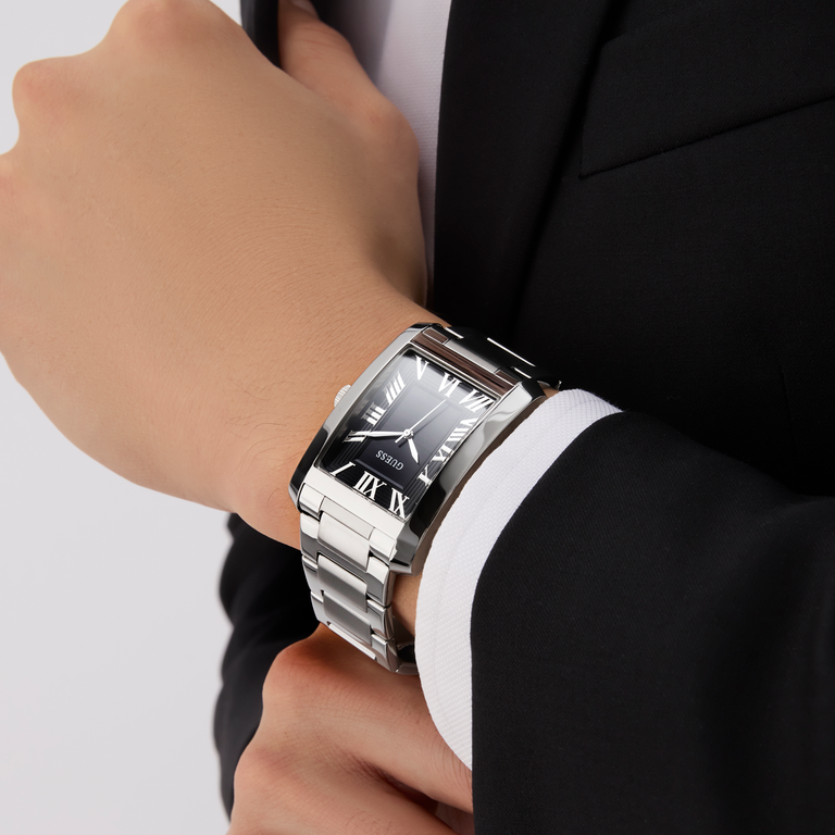 Silver watch on a person's wrist with a suit sleeve, on a light gray background
