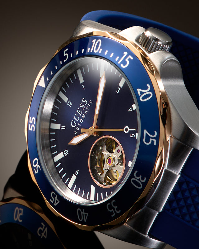 Close-up of a Guess Automatic wristwatch with a blue dial, blue bezel, blue strap, and silver-toned case with gold-tone accents.