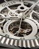 Close-up of a GUESS Automatic skeleton watch dial showing silver-toned gears, hands, and internal mechanical components through an open case.