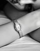 A close-up black and white photo of a woman's wrist wearing a GUESS watch with a textured metal link bracelet and an oval face.