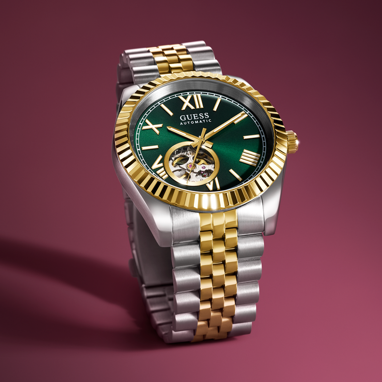 Luxury Guess watch with green dial and silver and gold band on a red background