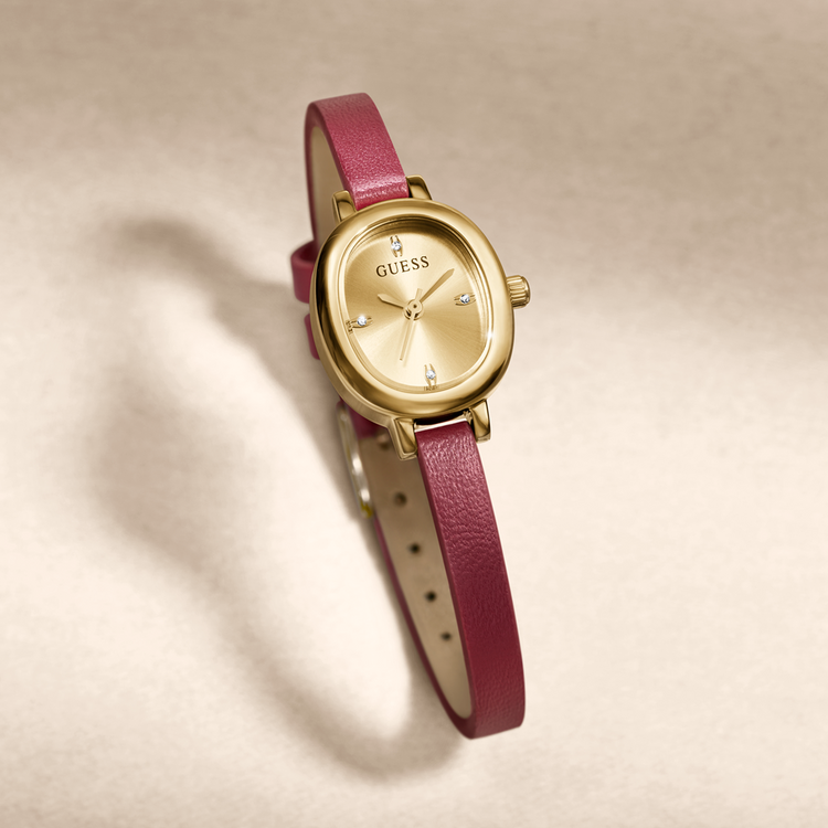 A GUESS women's watch featuring a gold-tone oval case, gold dial with crystal hour markers, and a textured magenta pink leather strap, shown on a neutral beige background.