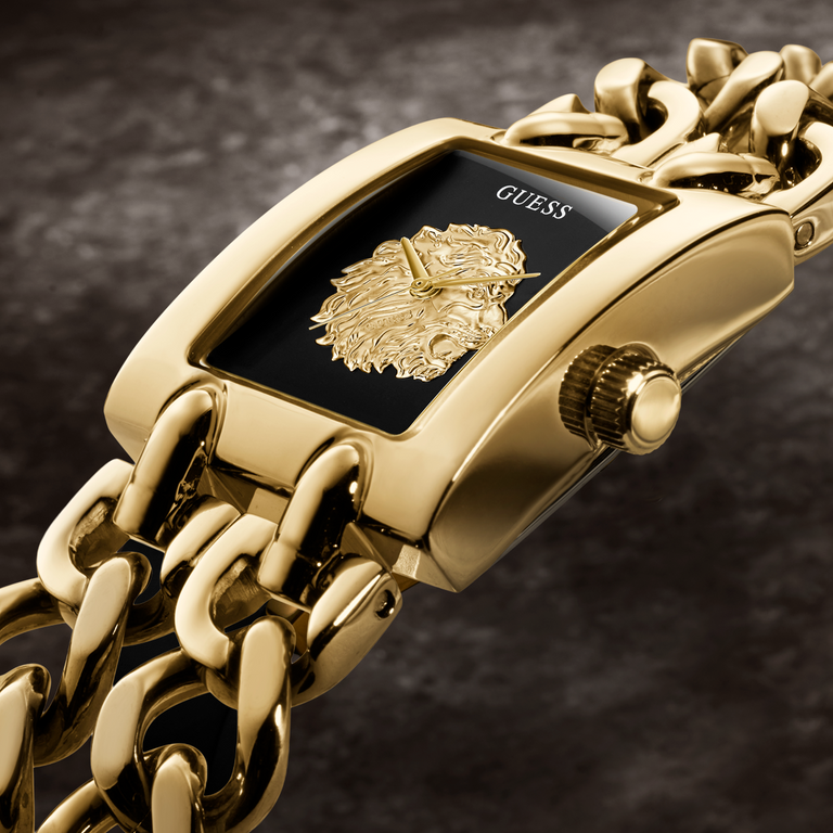Gold-tone Guess wristwatch with a rectangular black dial, lion emblem, and matching gold chain bracelet on a dark textured background.