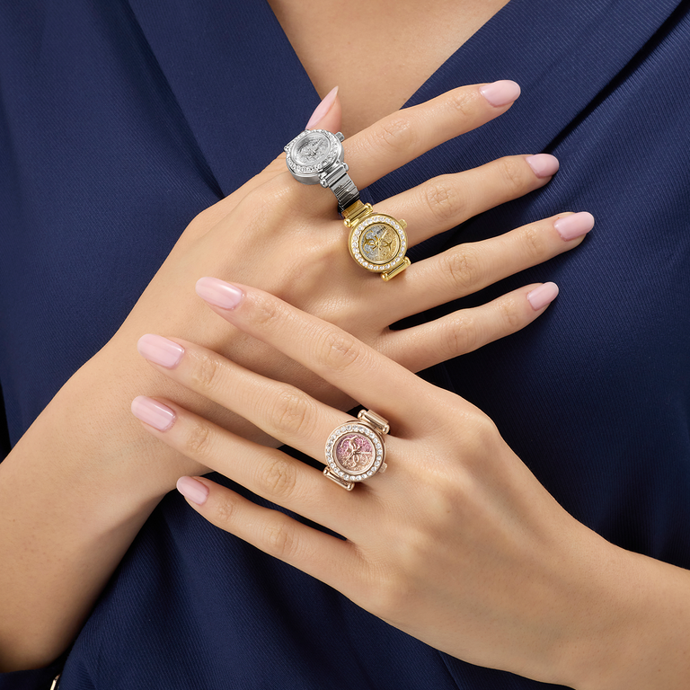 Three diamond watch rings on a person's fingers against a dark blue background