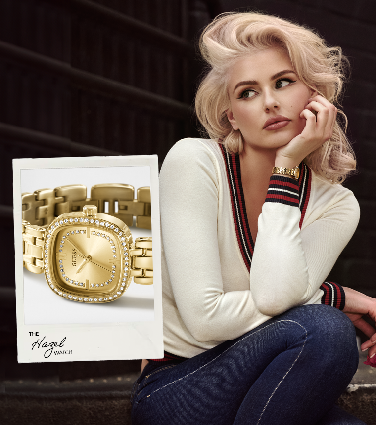 A blonde woman sits on dark steps wearing a gold-tone Gucci watch with a rhinestone-embellished bezel and a matching gold bracelet. A printed product inset on the left shows the watch clearly against a white card, while the model wears a cream sweater and dark jeans.