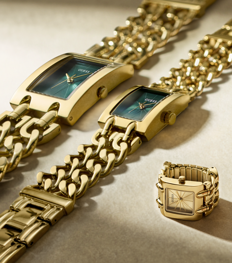 Three gold-tone GUESS wristwatches with matching curb-link bracelets are arranged diagonally on a beige surface, with one watch shown disassembled in the lower right corner.