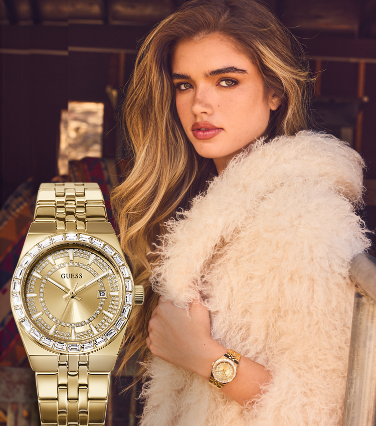 A woman in a fluffy cream faux-fur coat wears a gold-tone Guess watch, with a larger close-up of the same watch overlaid on the left side. The watch has a gold case, gold dial, crystal-embellished bezel, and matching gold link bracelet.