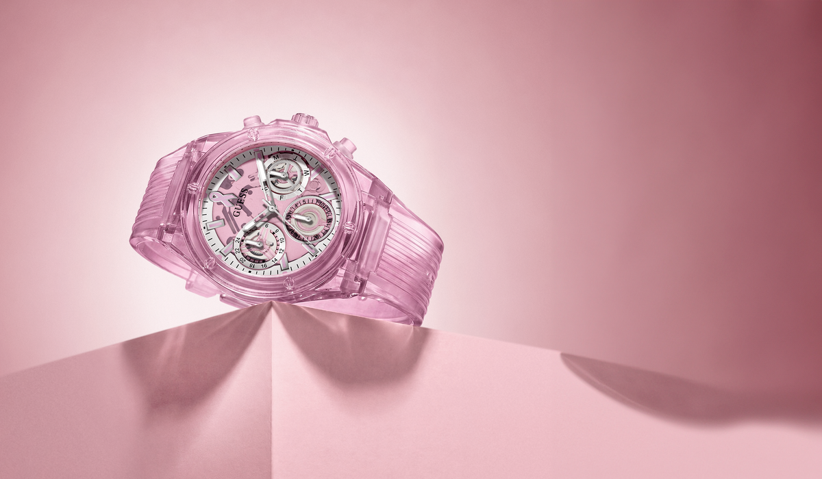 A translucent pink chronograph watch with a matching pink strap, resting on a pink surface against a pink background.