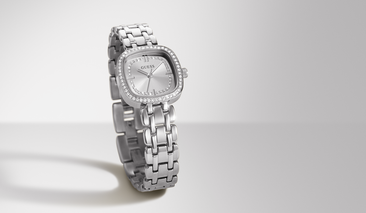 A silver-tone stainless steel women's watch with a square bezel set with small clear crystals, a silver dial, and a matching link bracelet, shown on a light gray studio background.