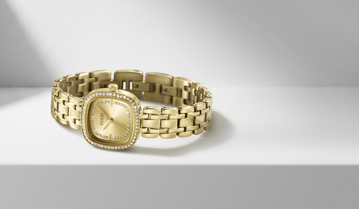 A gold-tone women's watch with a square bezel, crystal-encrusted edges, and a matching gold-tone link bracelet, displayed on a light gray surface.