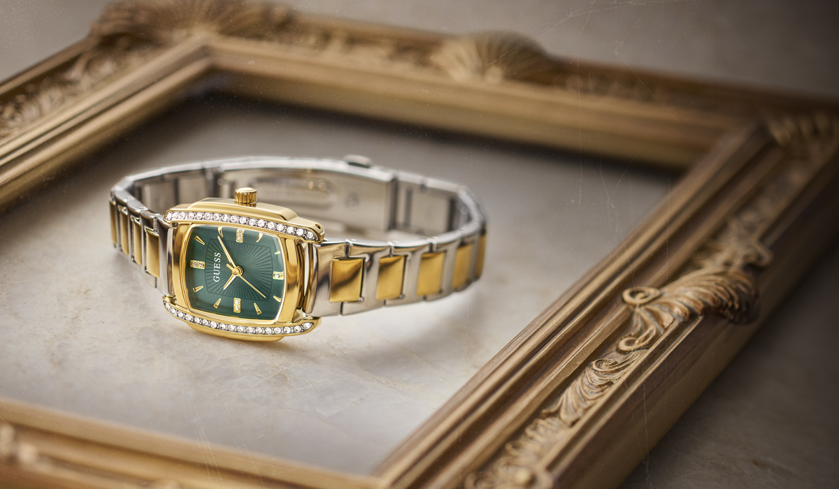 A two-tone gold and silver watch with a green dial and diamond accents, resting inside an ornate gold picture frame.