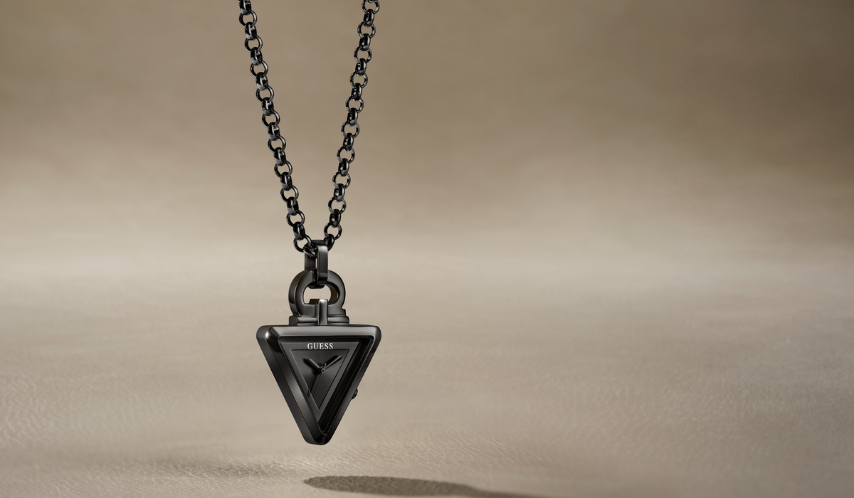 A black triangular pendant necklace with a textured geometric design and a matching black chain, suspended against a warm beige background.