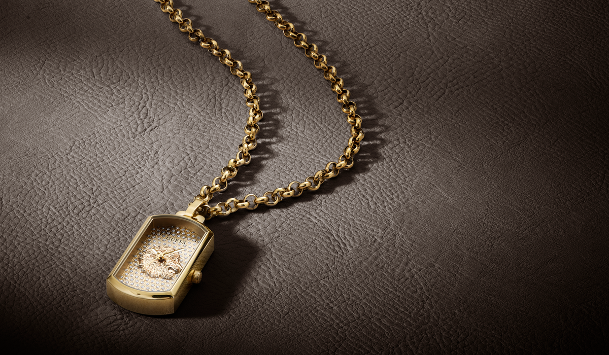 A gold rectangular pendant watch necklace with a textured gold chain, displayed on a dark brown leather background.